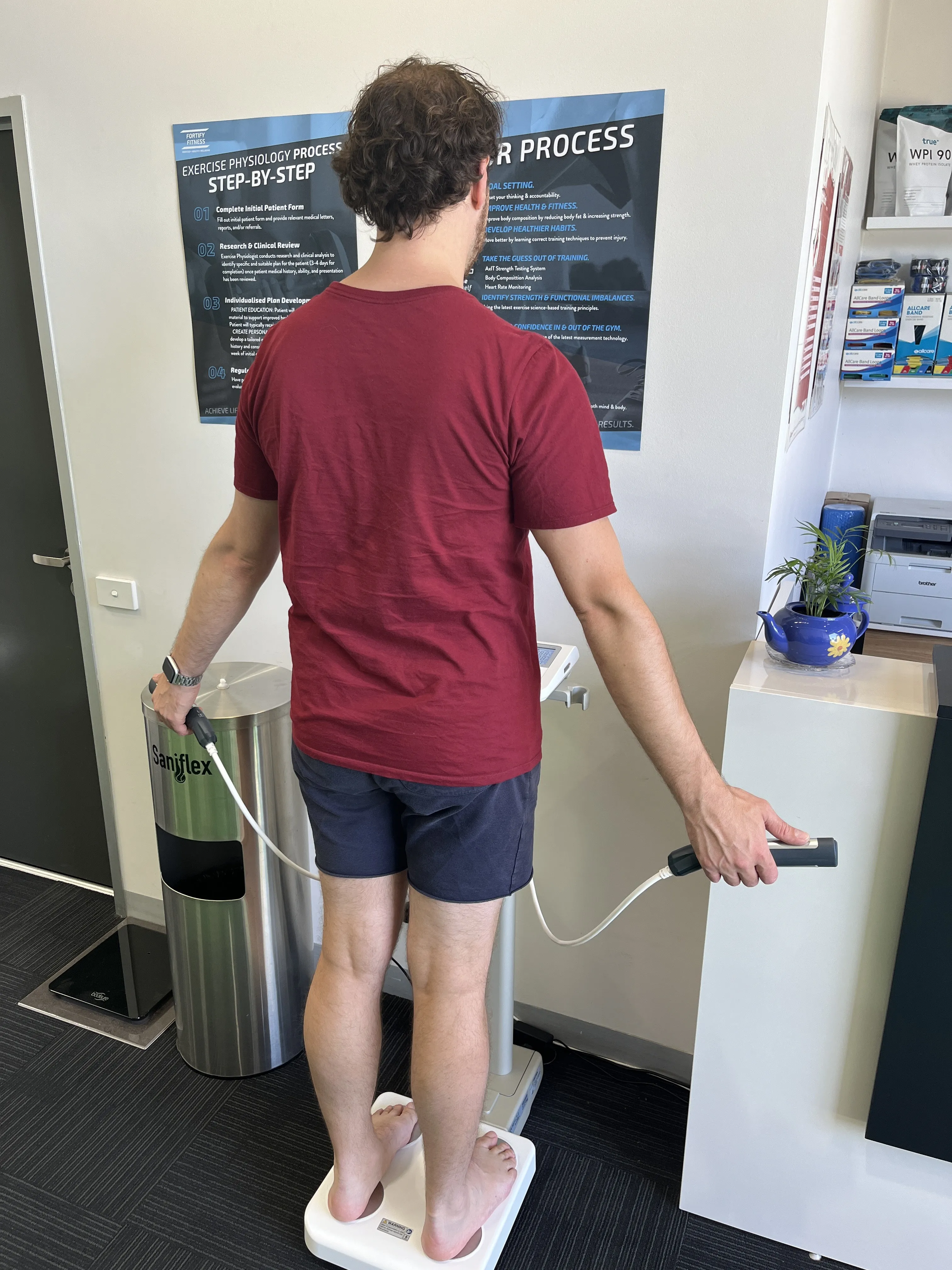Man standing on a weighing scale while holding hand grips in a clinic.